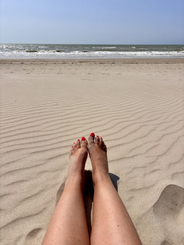De voeten van een vrouw in het zand met de zee op de achtergrond in een bohemian vibe voor het tarot merk LE BOHO