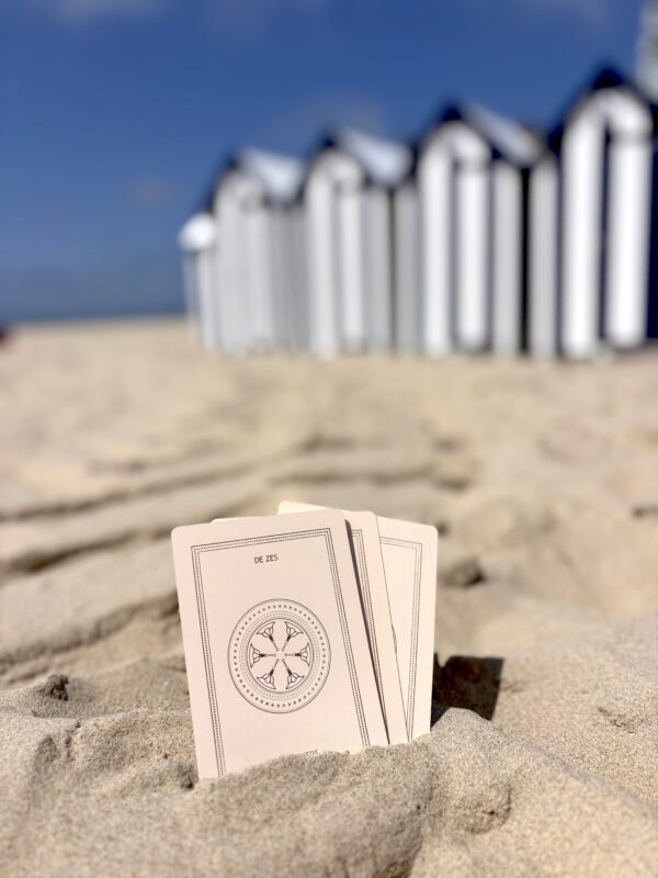 Set tarotkaarten met gouden details in boho zand met strandcabines op achtergrond, wat het een mooi cadeau maakt