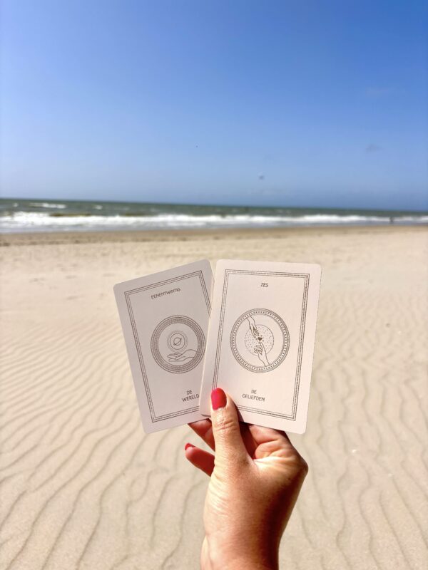 Vrouw houdt luxe tarotkaarten vast met de zee en het strand op de achtergrond